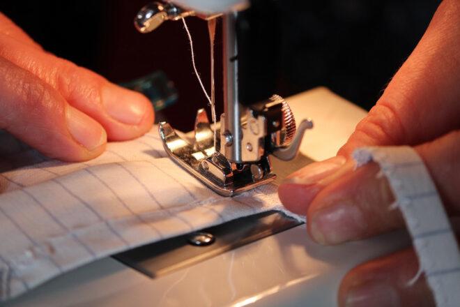 person using sewing machine to make fabric mask