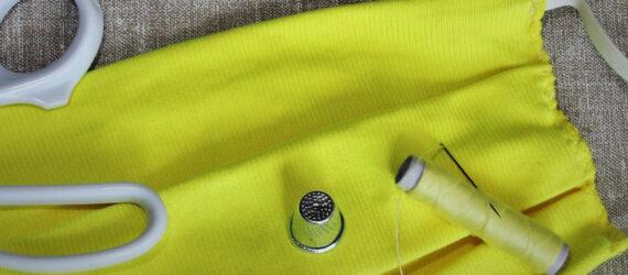 yellow homemade face mask near scissors, sewing needles and thread