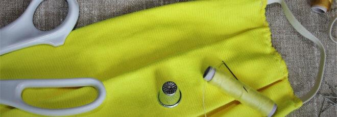 yellow homemade face mask near scissors, sewing needles and thread