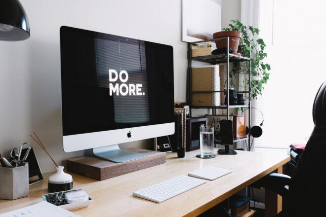 large desktop computer with background that reads, "Do More" next to shelf of plants