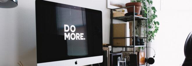 large desktop computer with background that reads, "Do More" next to shelf of plants