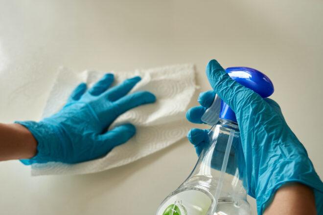 person wearing blue gloves while cleaning with spray bottle and paper towels