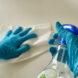 person wearing blue gloves while cleaning with spray bottle and paper towels