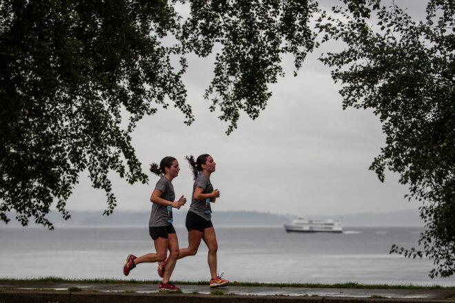 two people running beside waterfront with boats
