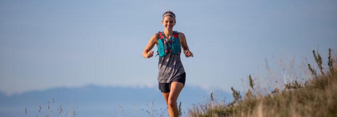 person running and smiling with ocean and mountains in background