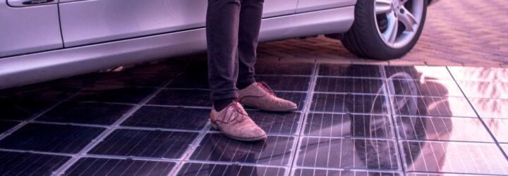 person standing next to solar tiles in a driveway with a parked silver car