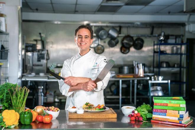man in white chef coat holding a knife and a spatula near cutting board and cookbooks
