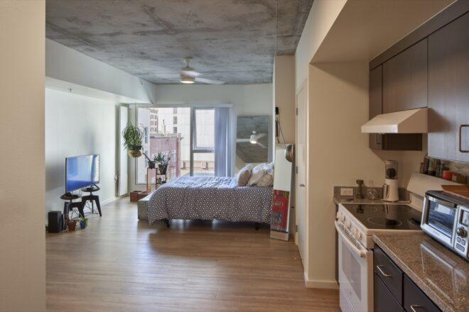 studio apartment with small kitchen and large bed and plenty of windows