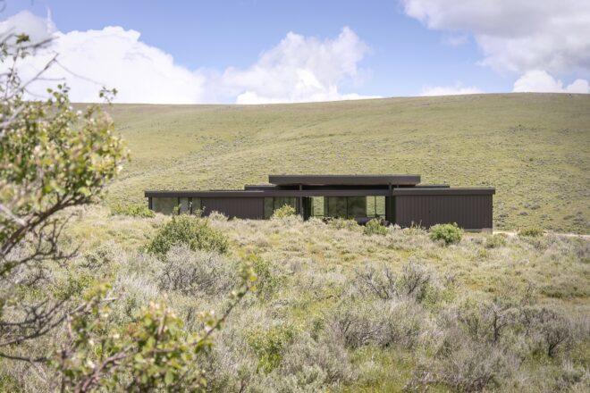 elongated black home on rolling green hills