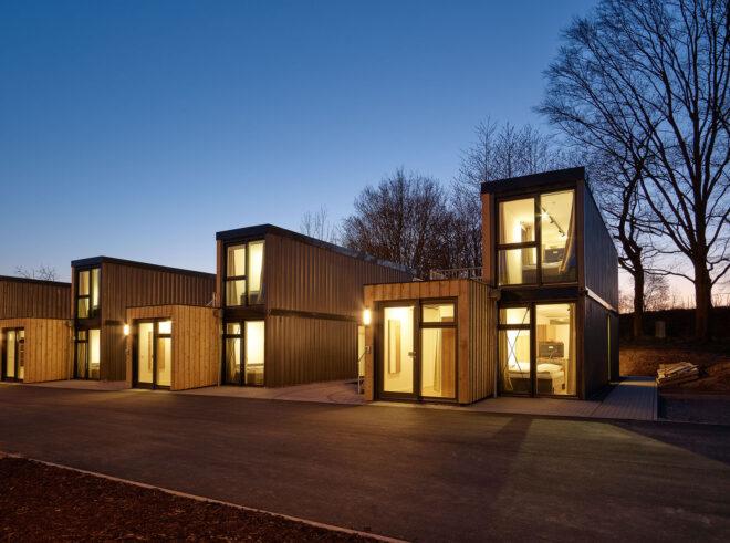 an evening shot of timber paneled micro-apartments lit up from within