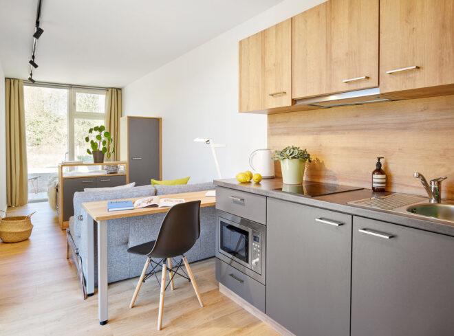 the interior of an apartment, showcasing light-colored wood accents and cabinets, and a sitting area