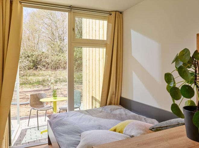 a bedroom with a large floor-to-ceiling window that lets in natural light