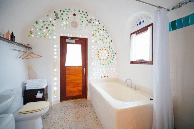 white bathroom with soaking tub and glass bottles arranged in ornate pattern in the wall