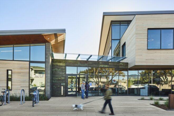 people walking past wood building with glass entrance