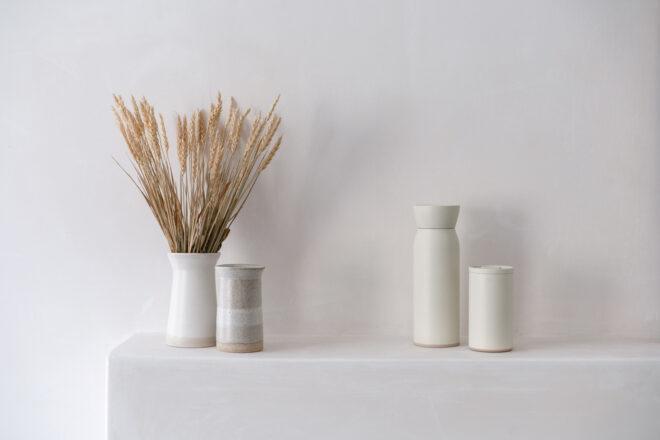 white water bottle and coffee cup next to tan vase and white vase full of wheat