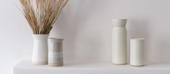 white water bottle and coffee cup next to tan vase and white vase full of wheat