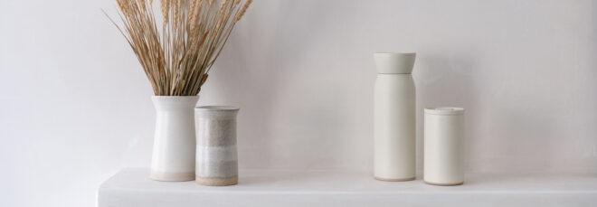 white water bottle and coffee cup next to tan vase and white vase full of wheat