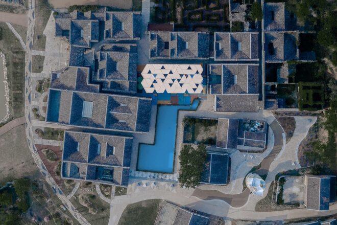 aerial rendering of large building with triangular glass roof tiles surrounded by ancient buildings