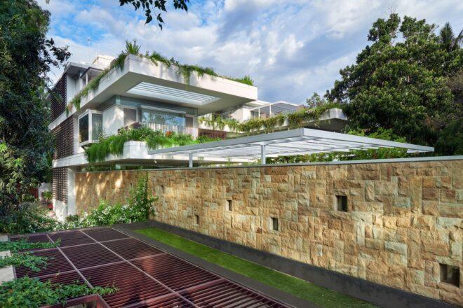 large stone wall around white home with hanging plants on the roof