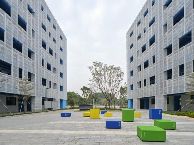 a school courtyard in between two buildings. colorful seating areas in blue, yellow and green are placed throughout the courtyard