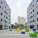 a school courtyard in between two buildings. colorful seating areas in blue, yellow and green are placed throughout the courtyard