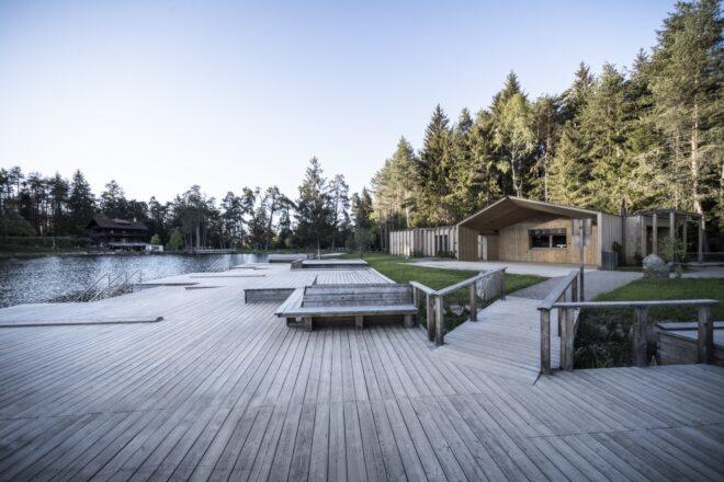 a wood dock area on a lake, with a lake house and trees to the right