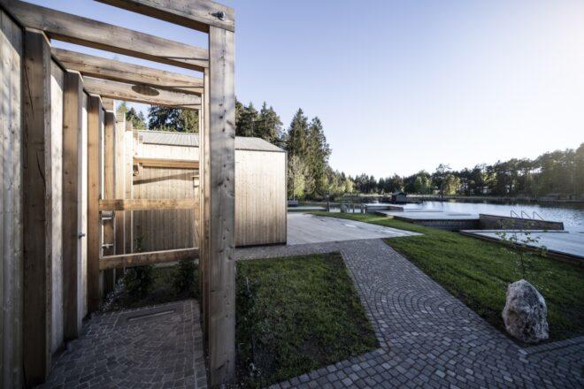 a lake house made of timber, with a stone path surrounded by grass leading toward it