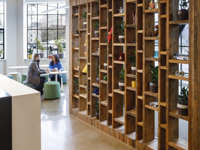 a tall, avant-garde brown bookcase. in the background, two people sit at a table together