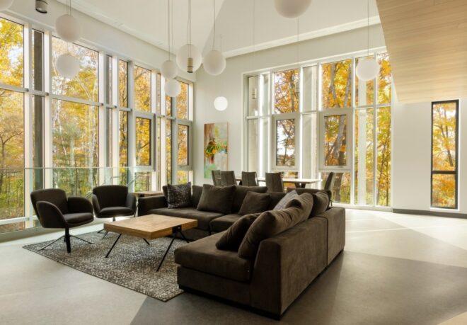 gray sectional sofa in white room with walls of windows revealing autumn leaves outside