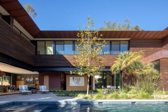 a two-level home with wood siding, a pool and trees outside