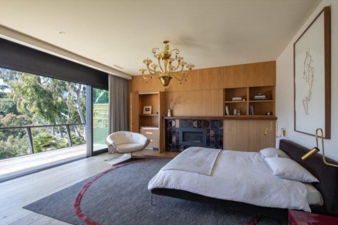 a bedroom with large windows, a chandelier-style light and wood cabinets