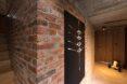 an exposed brick wall in a hallway feautring modern art and light-colored wood floors