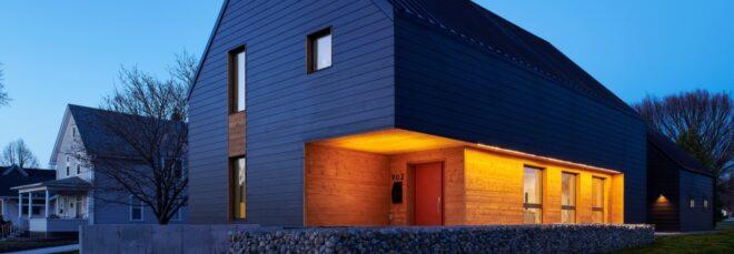 dark, gabled passive house with porch lights on at dusk