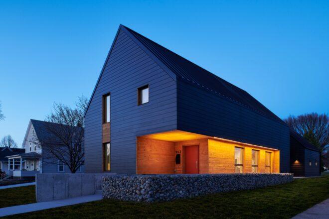 dark, gabled passive house with porch lights on at dusk
