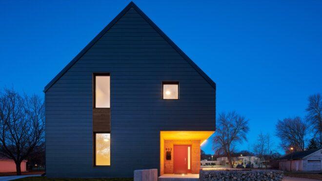 dark, gabled home with few windows lit up at dusk