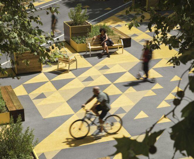 people riding bikes past small garden planters in a plaza