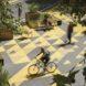 people riding bikes past small garden planters in a plaza