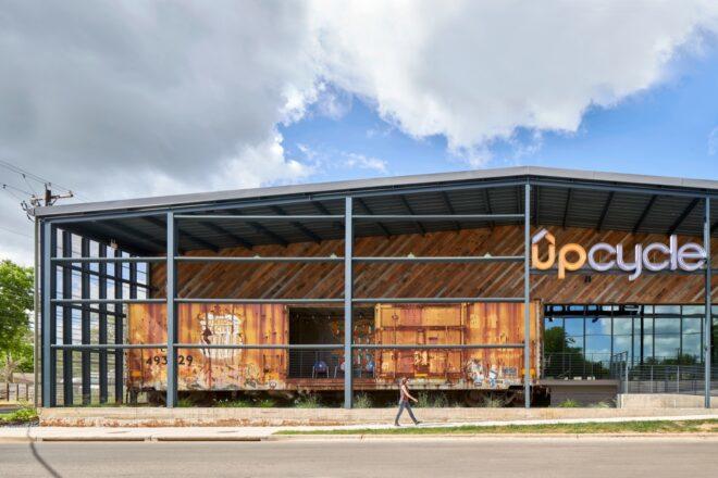weathered steel building with gabled roof and sign that says, "Upcycle"