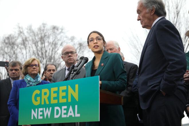 Representative Alexandria Ocasio-Cortez standing at a podium with a sign that reads, "Green New Deal"