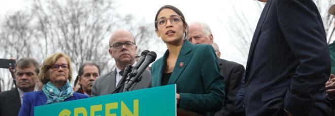 Representative Alexandria Ocasio-Cortez standing at a podium with a sign that reads, "Green New Deal"
