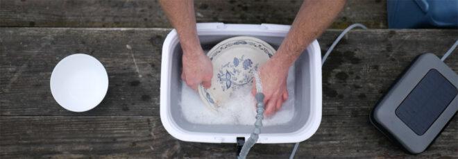 person washing dishes in a small, portable sink