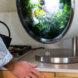 person using watering can to add water to base of a round indoor garden