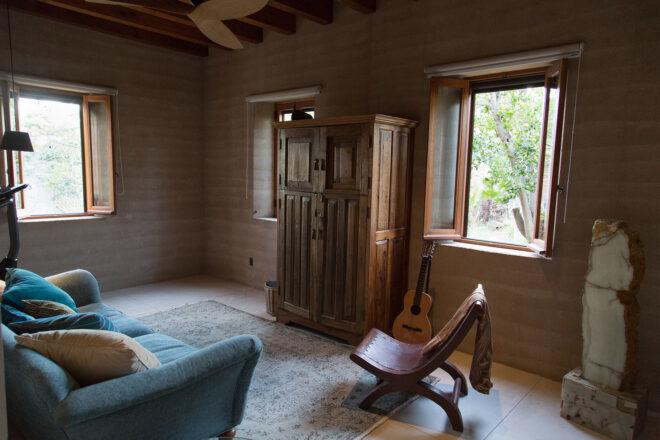 a sitting area with a blue chair and a smaller wood chair. two windows in the room are open