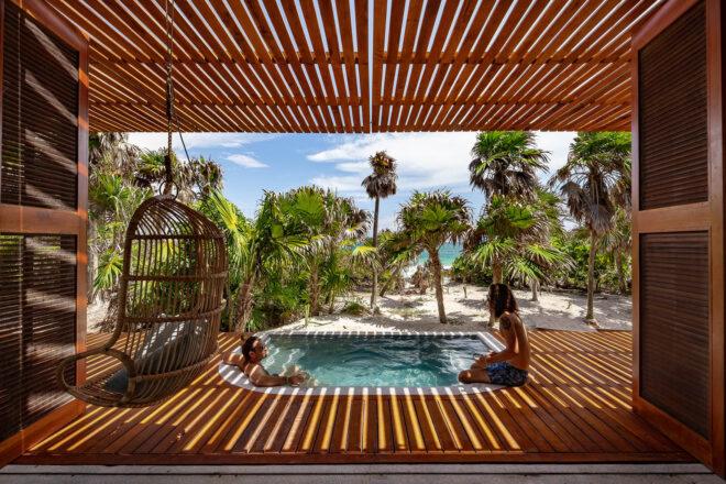 an indoor-outdoor area with wood accents, a hanging chair and an in-ground spa where two people are lounging