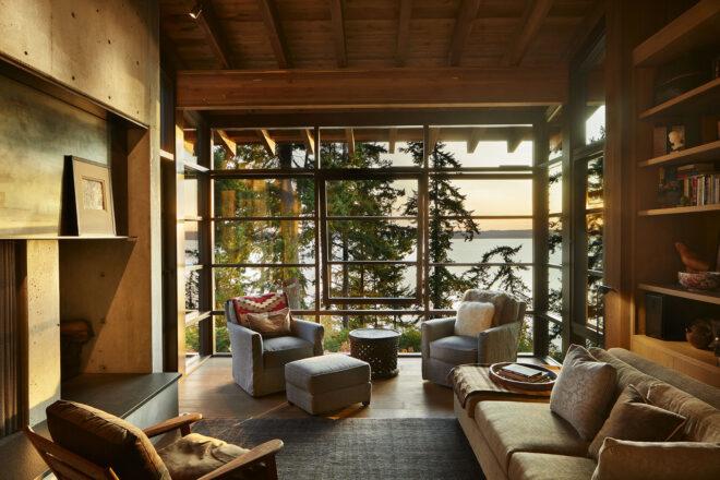 the inside of a home's living room with floor-to-ceiling windows and chairs and a sofa filling the room