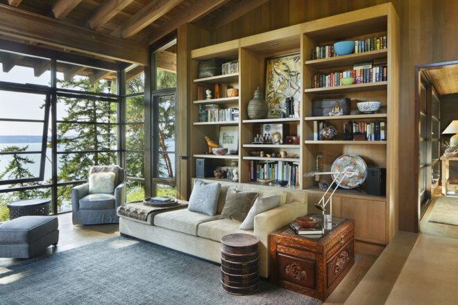 a living room with floor-to-ceiling windows, a bookshelf wall, chairs and a sofa filling the room