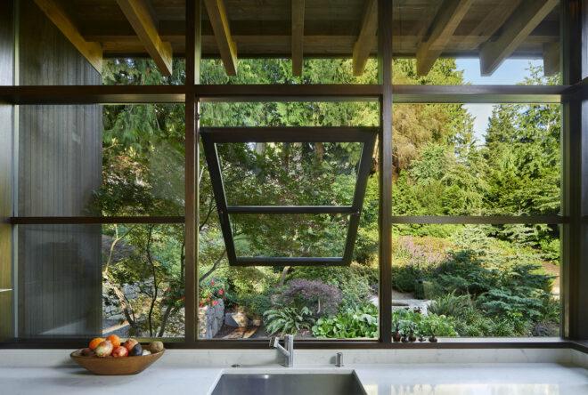 an open window in front of a sink that looks out on a greenery-filled yard