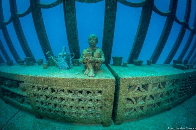 underwater greenhouse with statue of a child near a watering can