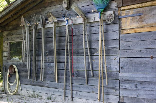 garden tools hanging on the side of a wooden shed