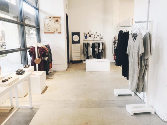 tables full of accessories and racks of gray and black dresses in front of a wall of windows